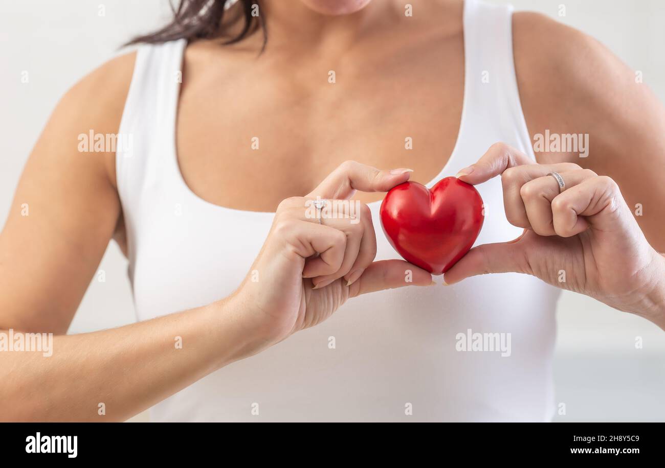 La femme tient un petit cœur rouge sur sa poitrine dans la région où le cœur réel est un symbole de prévention des maladies cardiaques. Banque D'Images