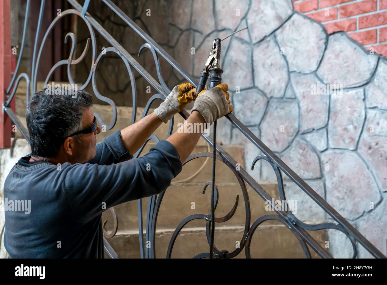 L'homme tient la machine à souder en main, se prépare à commencer le travail de soudage de pièces métalliques à la main courante d'escalier dans une maison privée. Banque D'Images