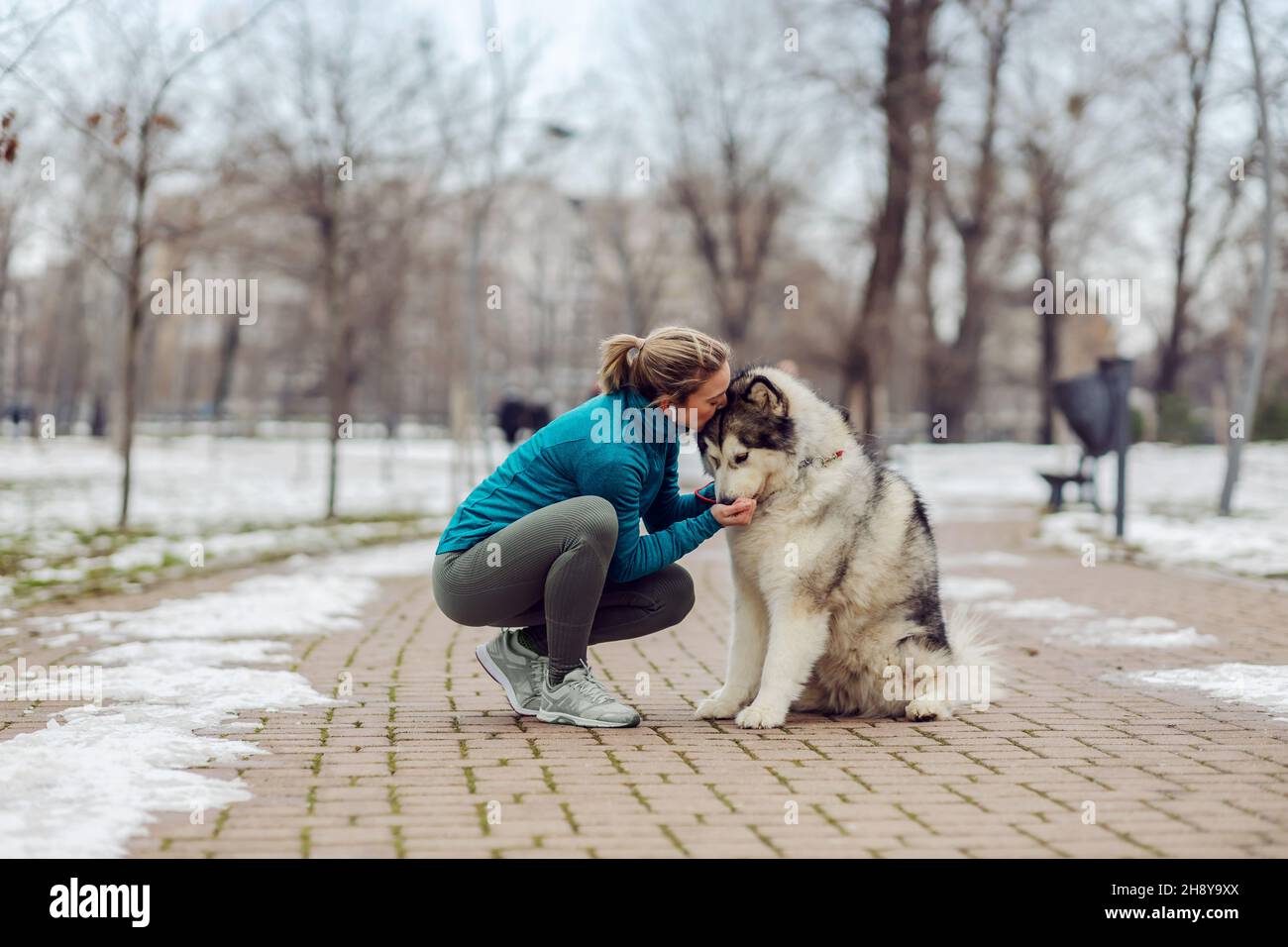 Sportswoman embrassant son chien et l'embrassant tout en se broutant dans le parc par temps neigeux.Animaux de compagnie, loisirs, activités de fin de semaine Banque D'Images