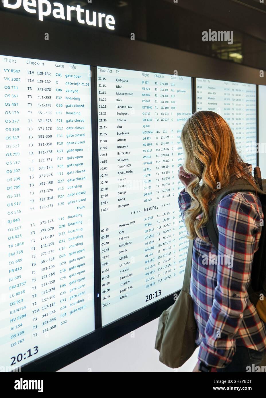 Jeune femme avec sac à dos vert et chemise regardant l'écran de départ à l'aéroport Banque D'Images