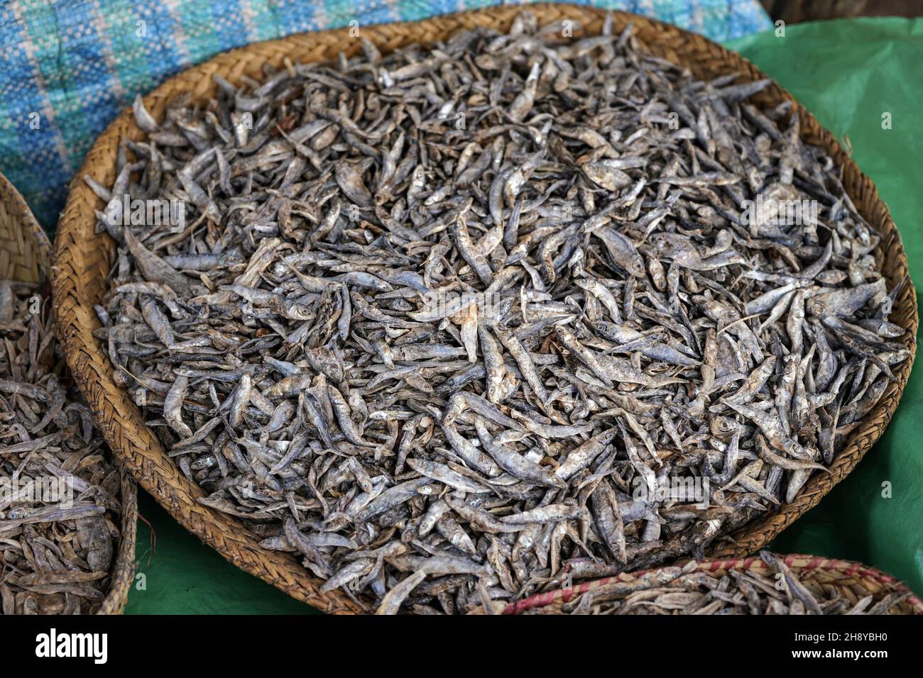 Petits poissons séchés exposés dans un panier de paille sur le marché alimentaire à Ranohira, Madagascar, détail de gros plan Banque D'Images