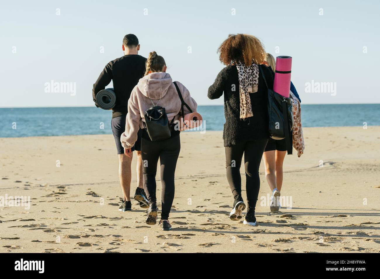 Arrière d'un groupe multiculturel marchant sur la plage avec des tapis et des sacs de yoga Banque D'Images