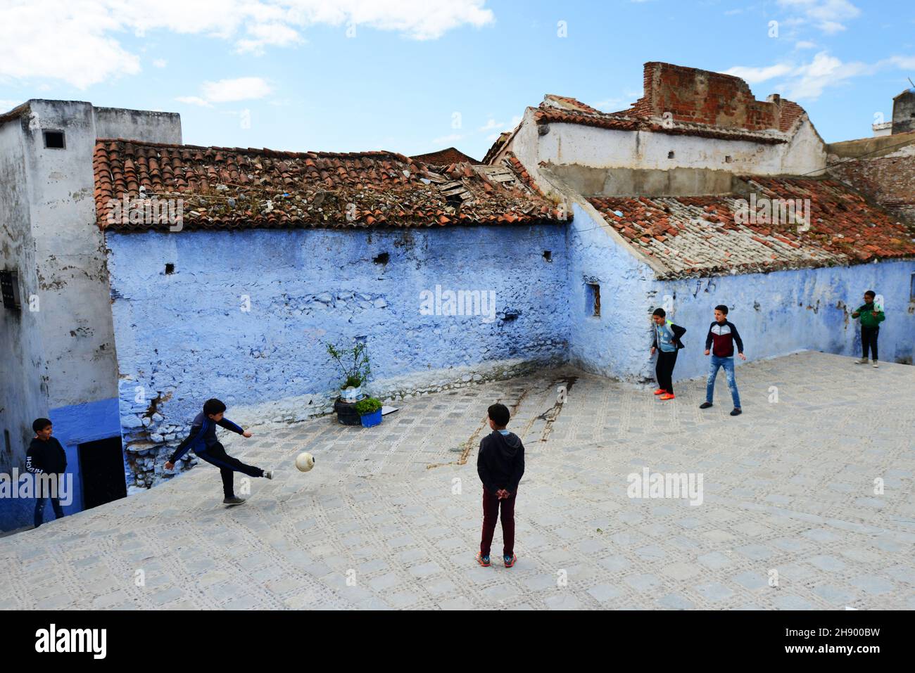 Des garçons marocains jouant au football entre les maisons peintes traditionnellement en bleu dans la médina de Chefchaouen, dans les montagnes de Rif, dans le nord du Maroc. Banque D'Images