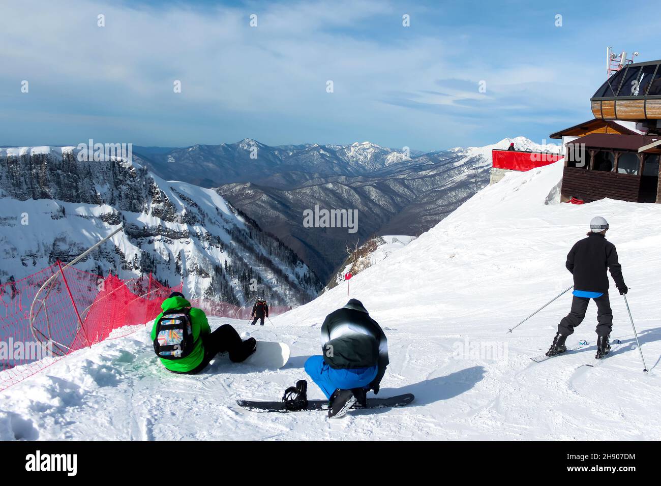 Au sommet de la piste de ski, les snowboarders s'enfilent sur leurs planches et les skieurs se mettent en route.En arrière-plan sont les chaînes de montagnes, le ciel bleu et le nuage Banque D'Images