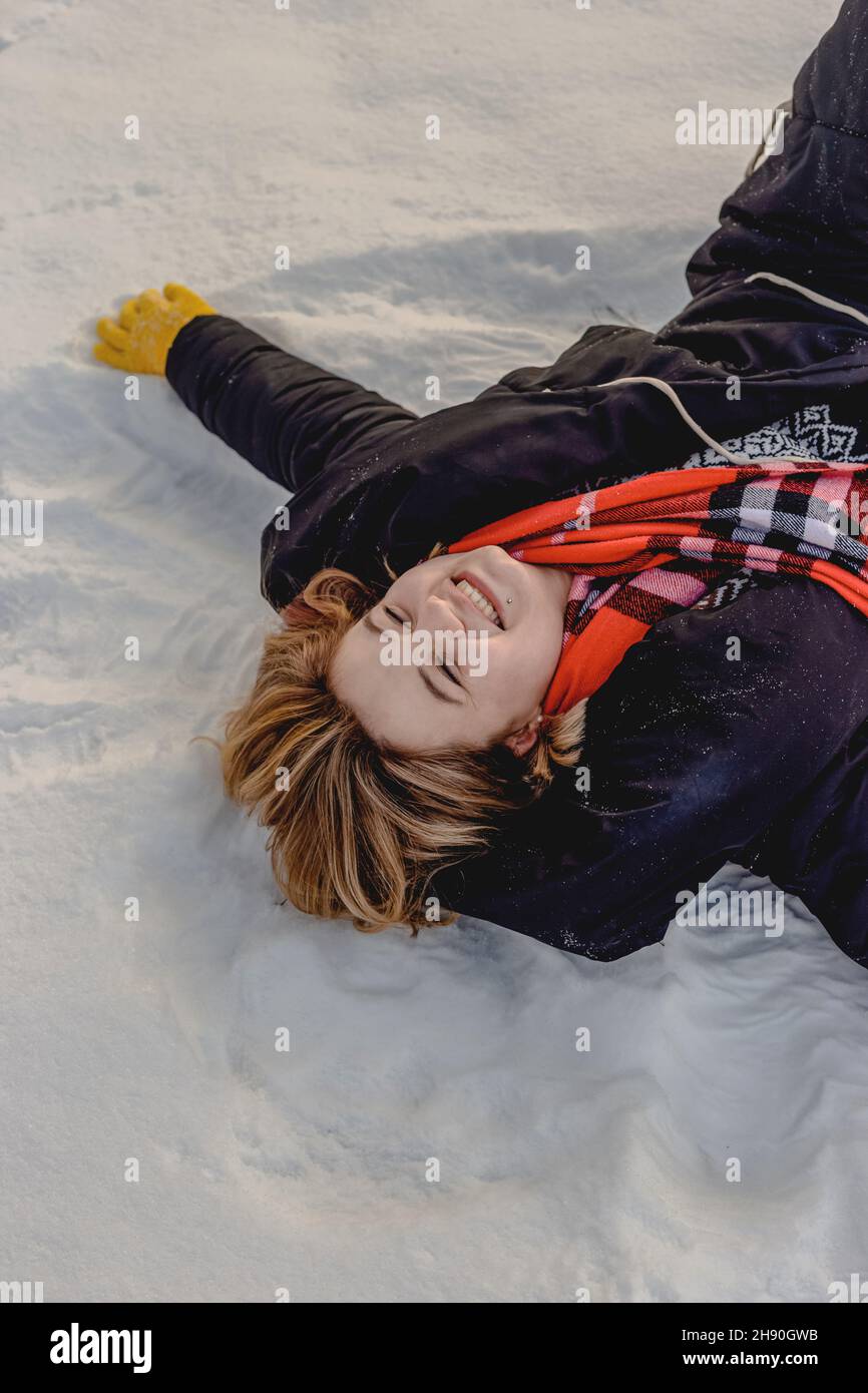 Bonne jeune femme blonde se trouve dans la neige, sous un manteau noir, une écharpe orange et des gants jaunes.Saison d'hiver.Gros plan Banque D'Images