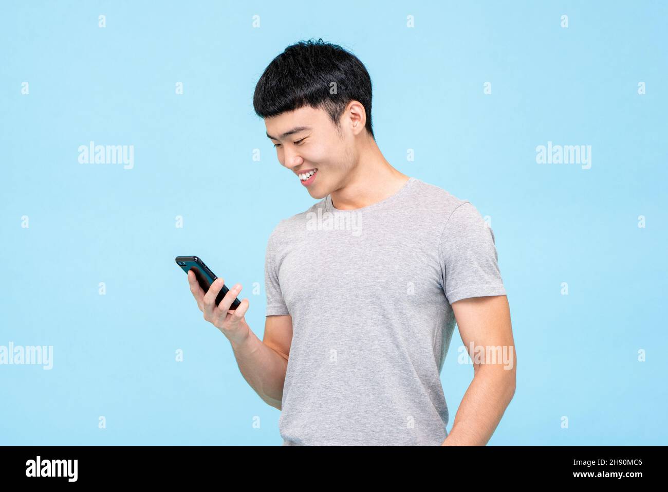 Jeune homme asiatique reconnaissant regardant un smartphone via les réseaux sociaux, isolé sur fond de studio bleu Banque D'Images