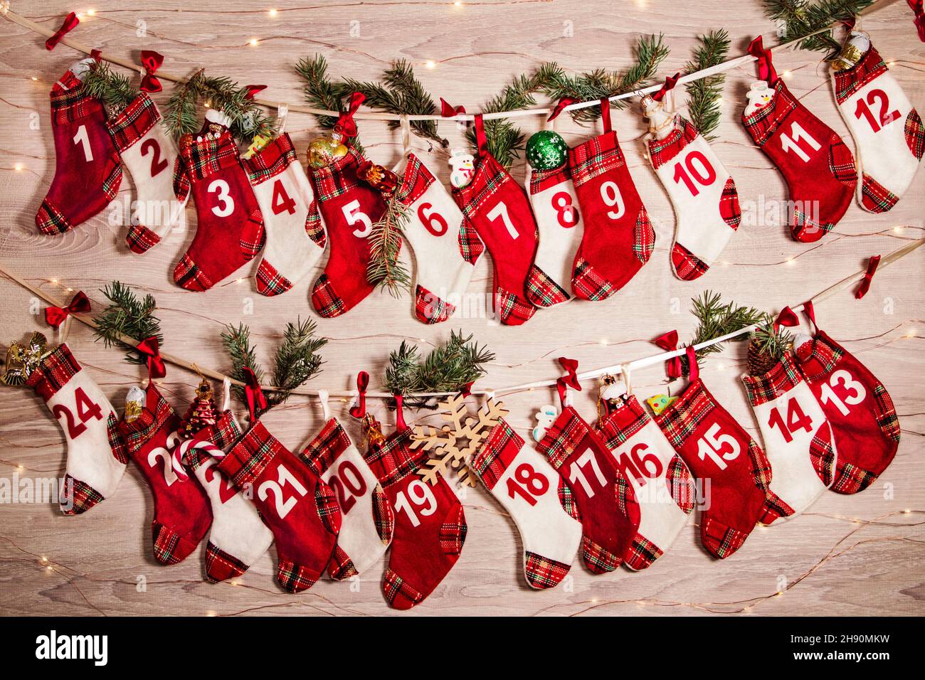 Calendrier de l'Avent avec des cadeaux dans des chaussettes pour enfants, des branches d'un arbre de Noël, des lumières de guirlandes sur un fond en bois.24 chaussettes de l'Avent calme Banque D'Images
