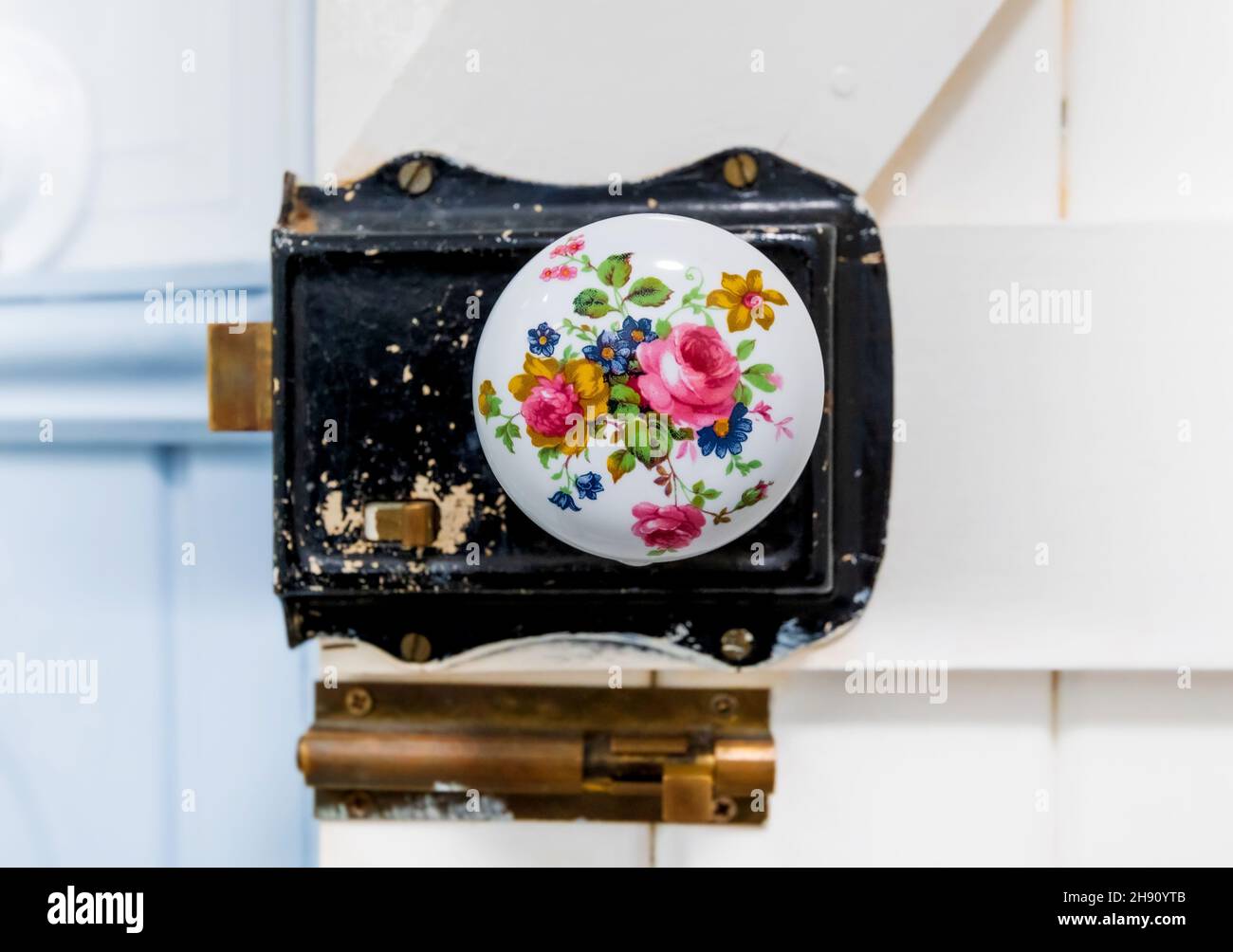 Gros plan sur une porte ronde en porcelaine de style victorien décorée de fleurs bouton sur une porte de style grange en bois blanc. Banque D'Images