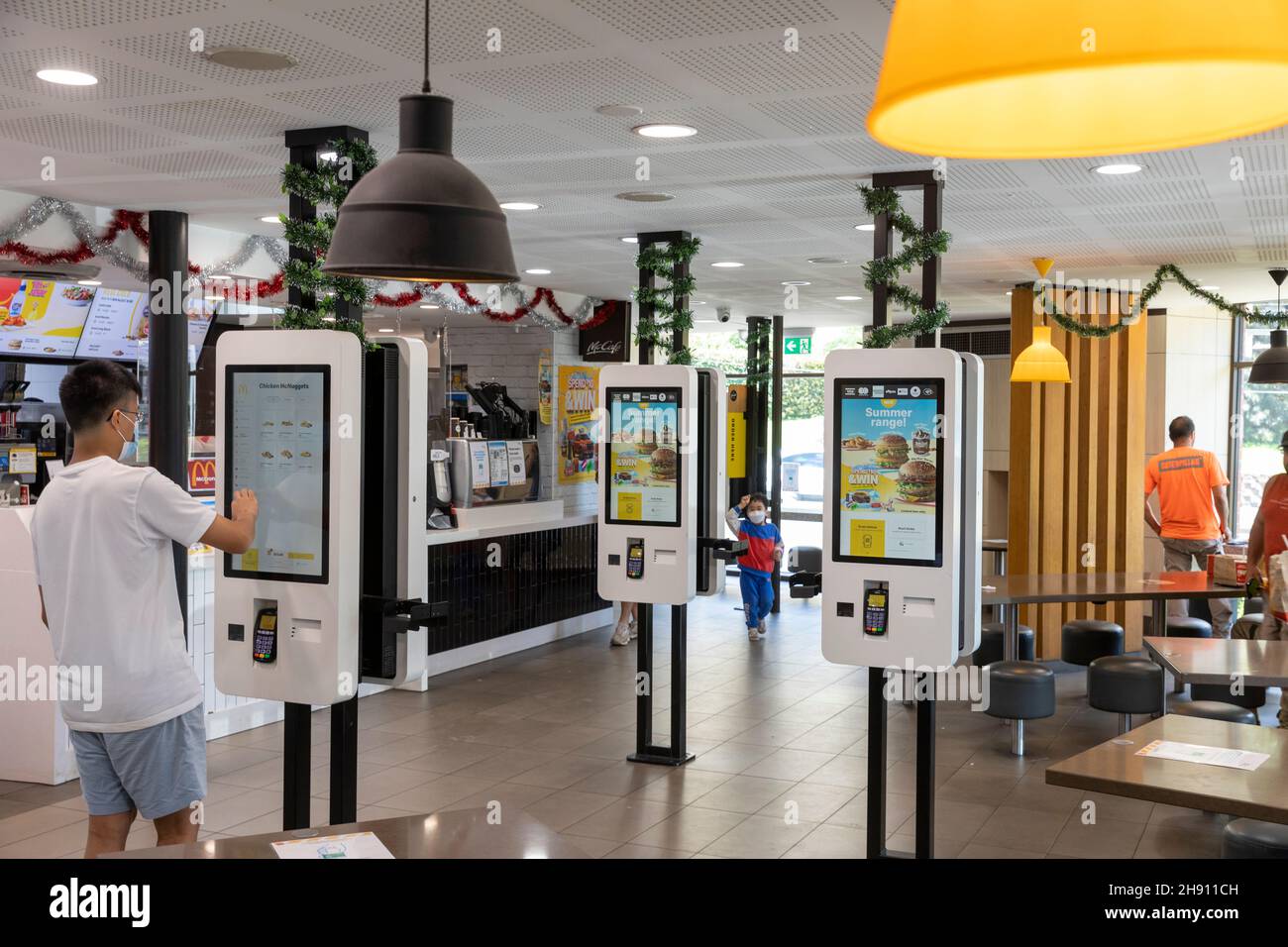 Jeune homme utilisant l'écran tactile électronique pour commander un repas McDonalds restaurant café à Sydney, faciemark en raison de la pandémie Covid 19 Banque D'Images