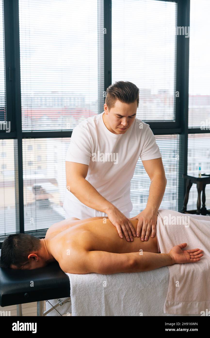 Cliché vertical d'un masseur professionnel masculin avec des mains fortes massant le dos à un sportif musclé allongé sur l'estomac. Banque D'Images