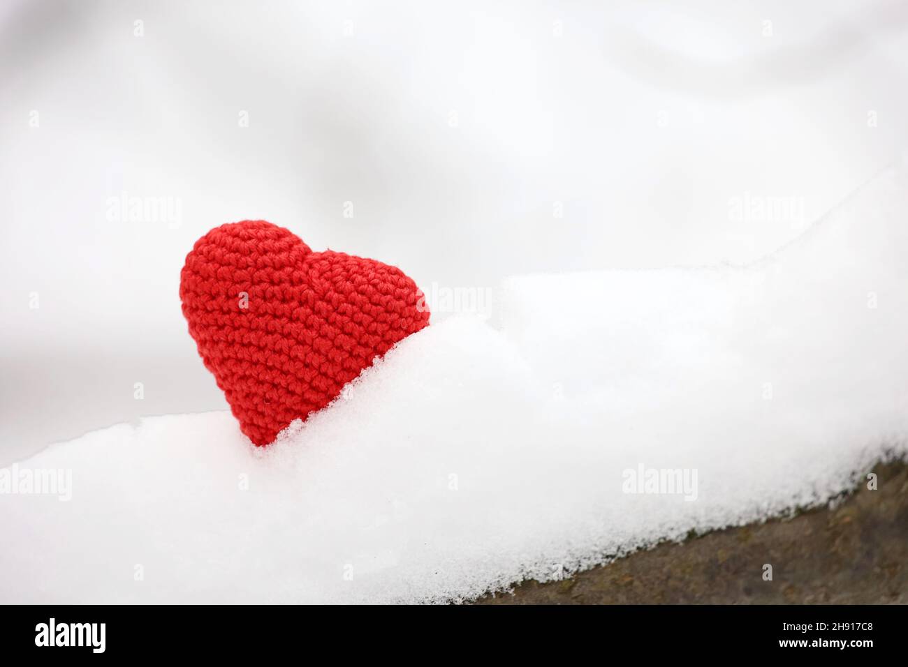 Coeur rouge tricoté dans la neige sur une branche d'arbre en forêt d'hiver.Carte de Saint-Valentin, symboles d'amour, fond pour la fête de Noël Banque D'Images