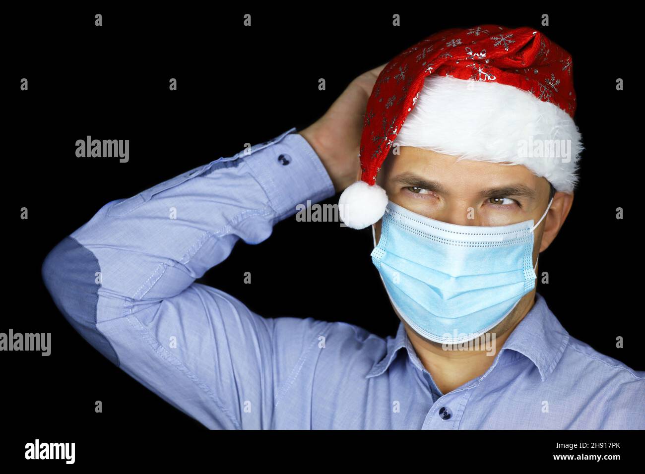 Portrait de l'homme en masque et chapeau de père Noël sur fond noir.Fête de Noël, jour férié du nouvel an pendant la pandémie du coronavirus Banque D'Images