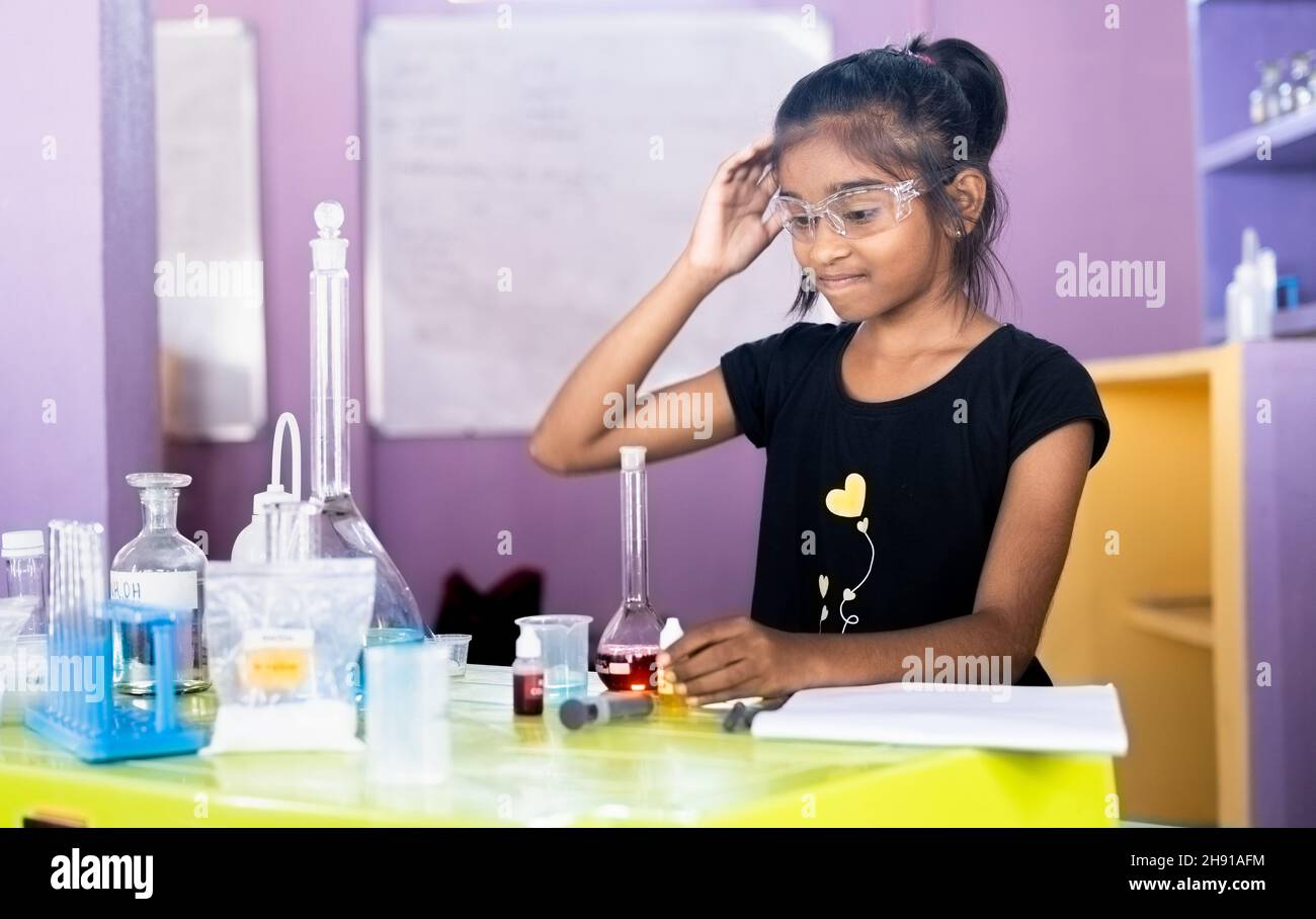 Confondu fille de gratter la tête en regardant les équipements de laboratoire au laboratoire de chimie tout en faisant l'expérience - concept de difficulté à apprendre à Banque D'Images