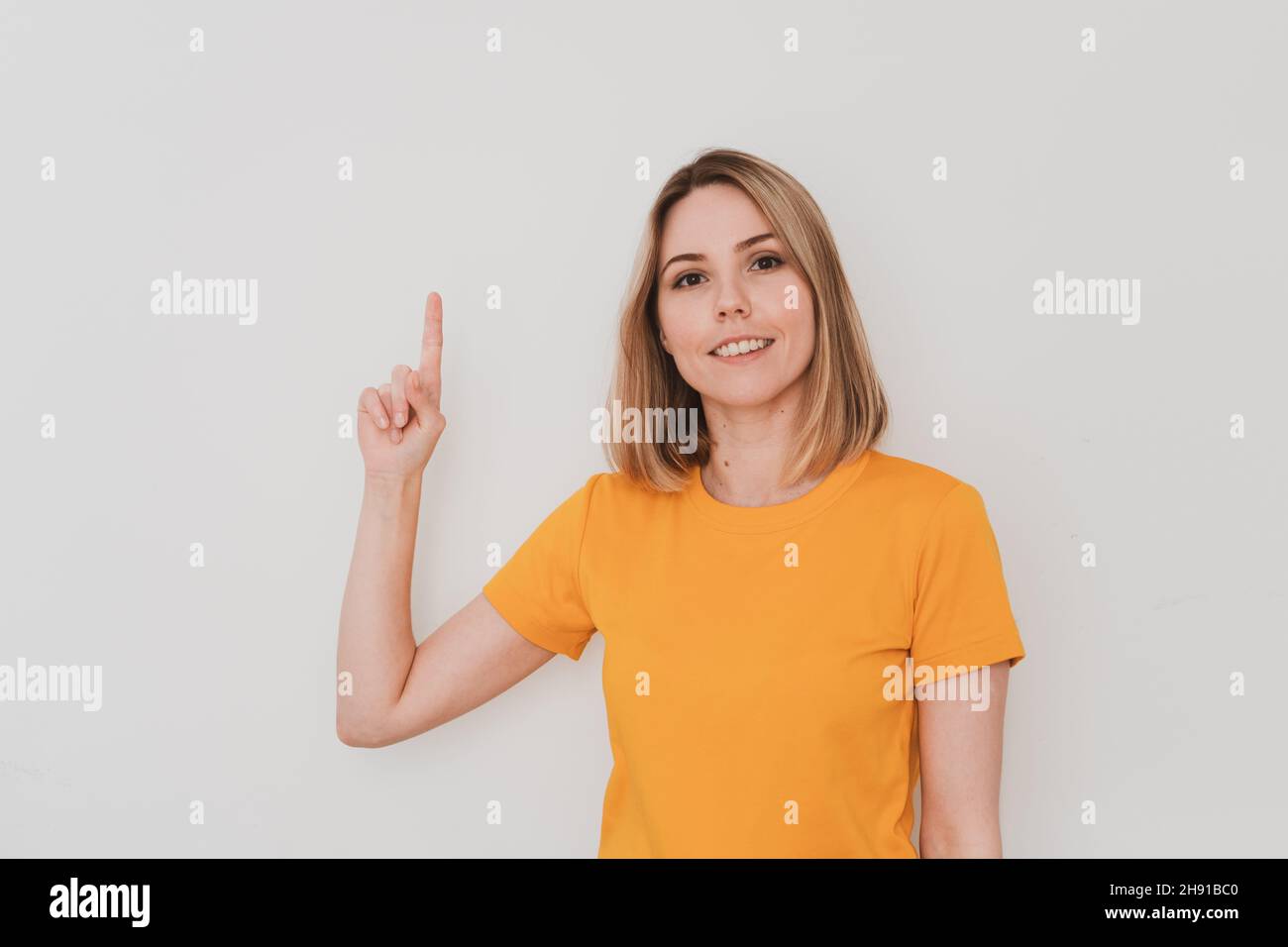 Portrait de la jeune femme en t-shirt jaune pointant son doigt vers le haut.Sur fond blanc.Mouvements de la main Banque D'Images