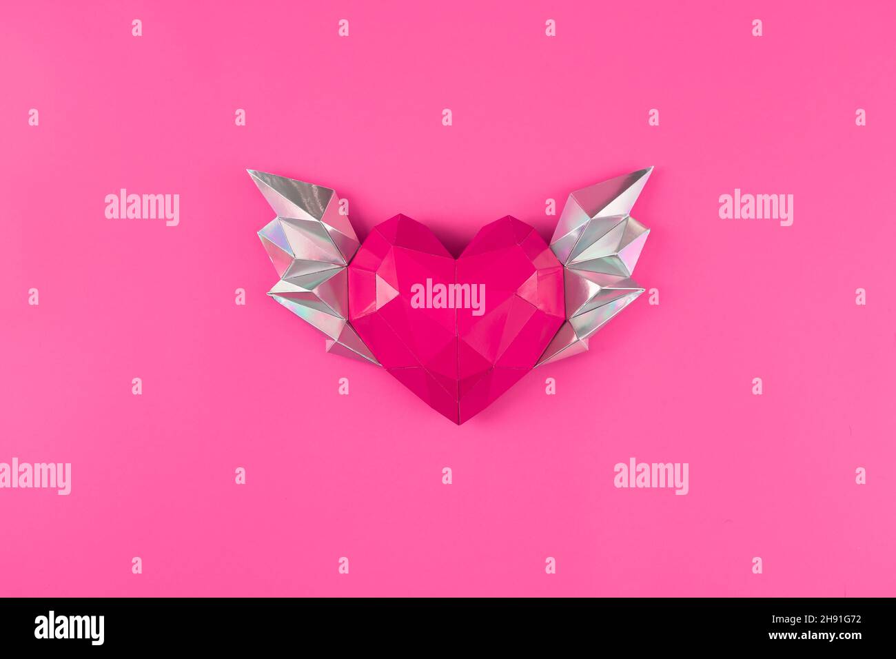Le coeur est polygonal, fait de papier avec des ailes sur un fond rose.Vue de dessus. Maquette Banque D'Images