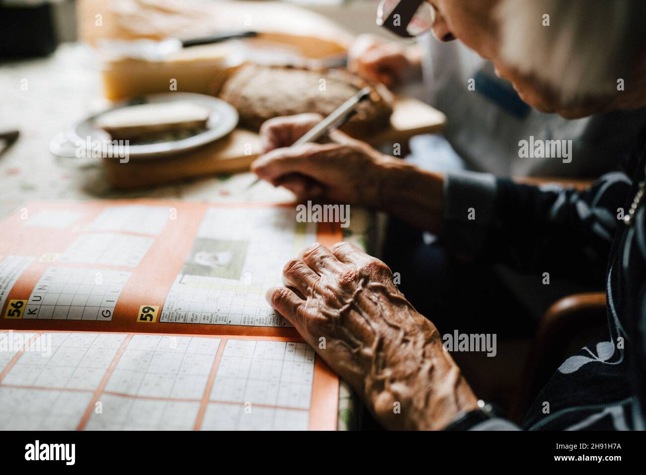 Image rognée d'une femme âgée résolvant des mots croisés dans un livre à la maison Banque D'Images