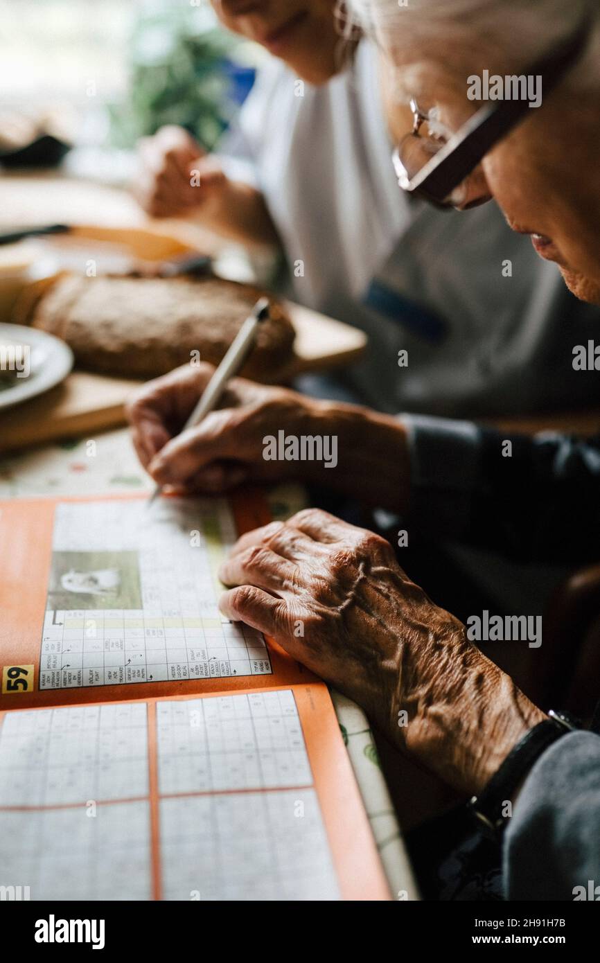 Femme sénior résolvant des mots croisés dans un livre à table Banque D'Images