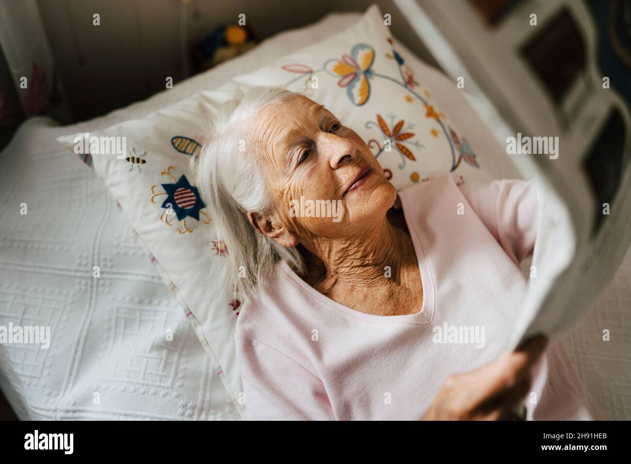 Vue en grand angle de la femme âgée qui lit des journaux pendant qu'elle est allongée sur le lit Banque D'Images