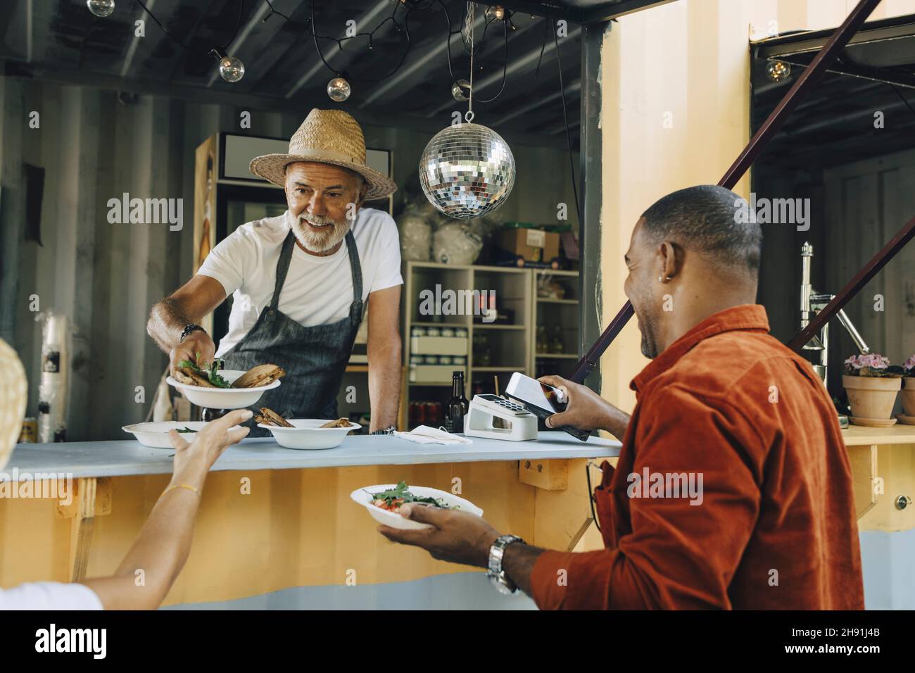 Vendeur servant de la nourriture pendant que le client masculin fait le paiement sans contact par téléphone intelligent Banque D'Images