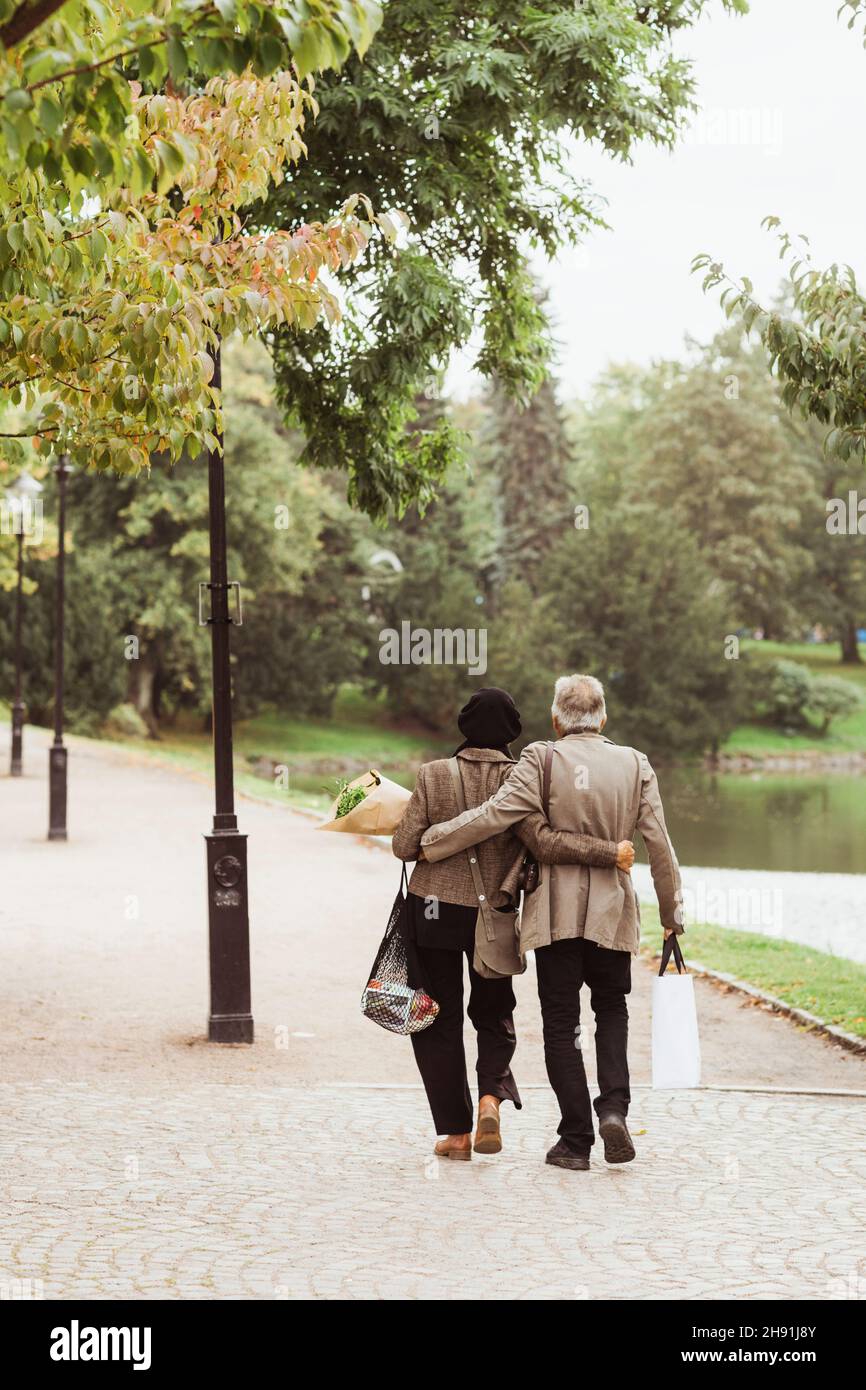 Vue arrière d'un couple âgé marchant avec les bras sur le sentier du parc Banque D'Images