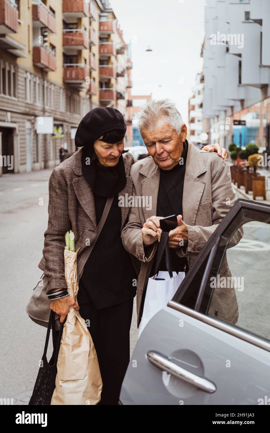 Couple âgé utilisant un smartphone en voiture dans la rue en ville Banque D'Images