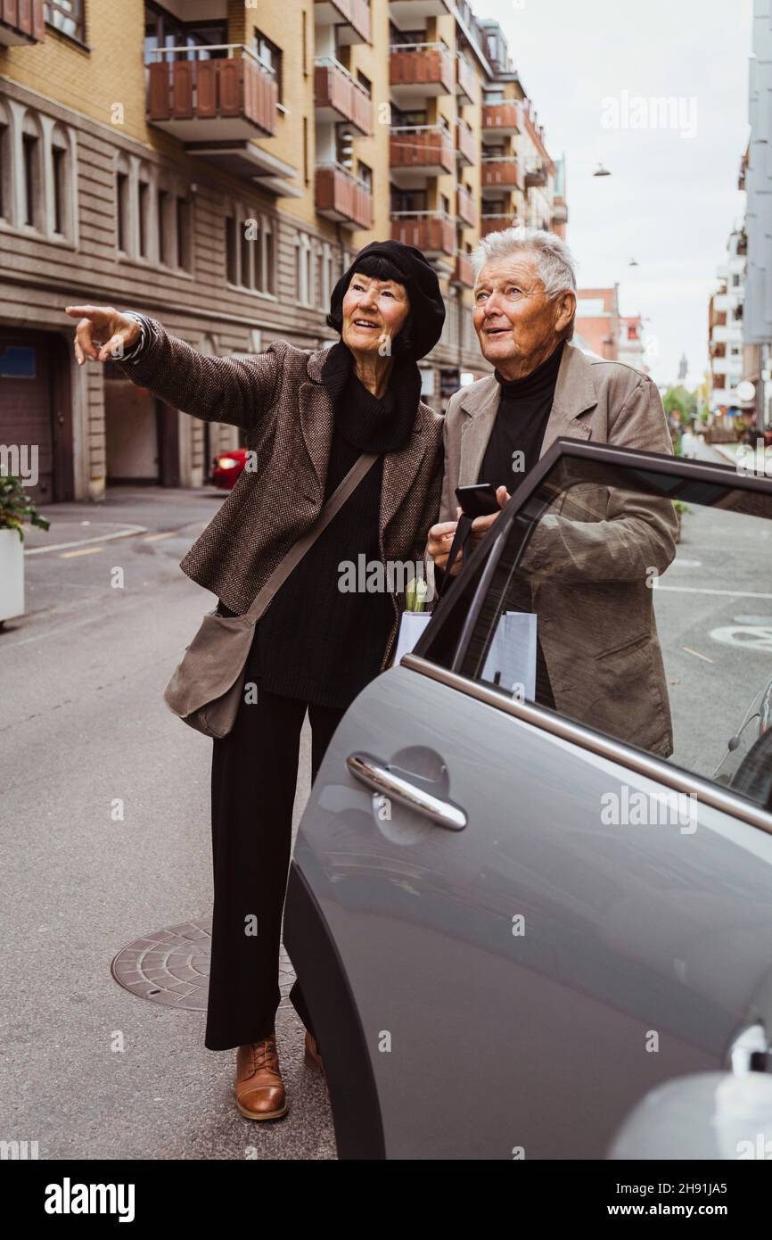 Une femme souriante se faisant remarquer alors qu'un homme âgé tient un smartphone en voiture dans la rue Banque D'Images
