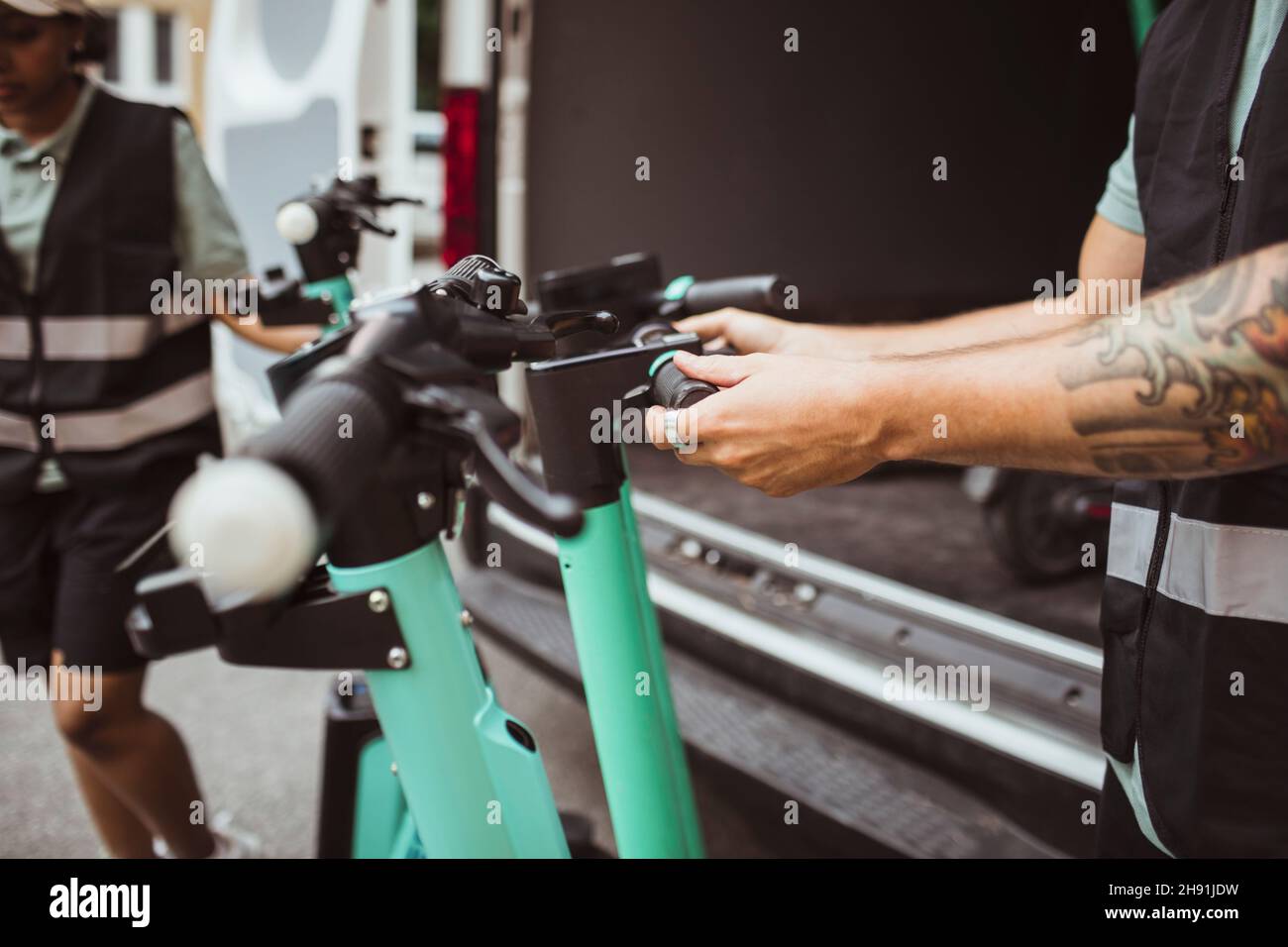 Section médiane de la livraison mâle tenant la poignée de poussée électrique du scooter par une camionnette Banque D'Images