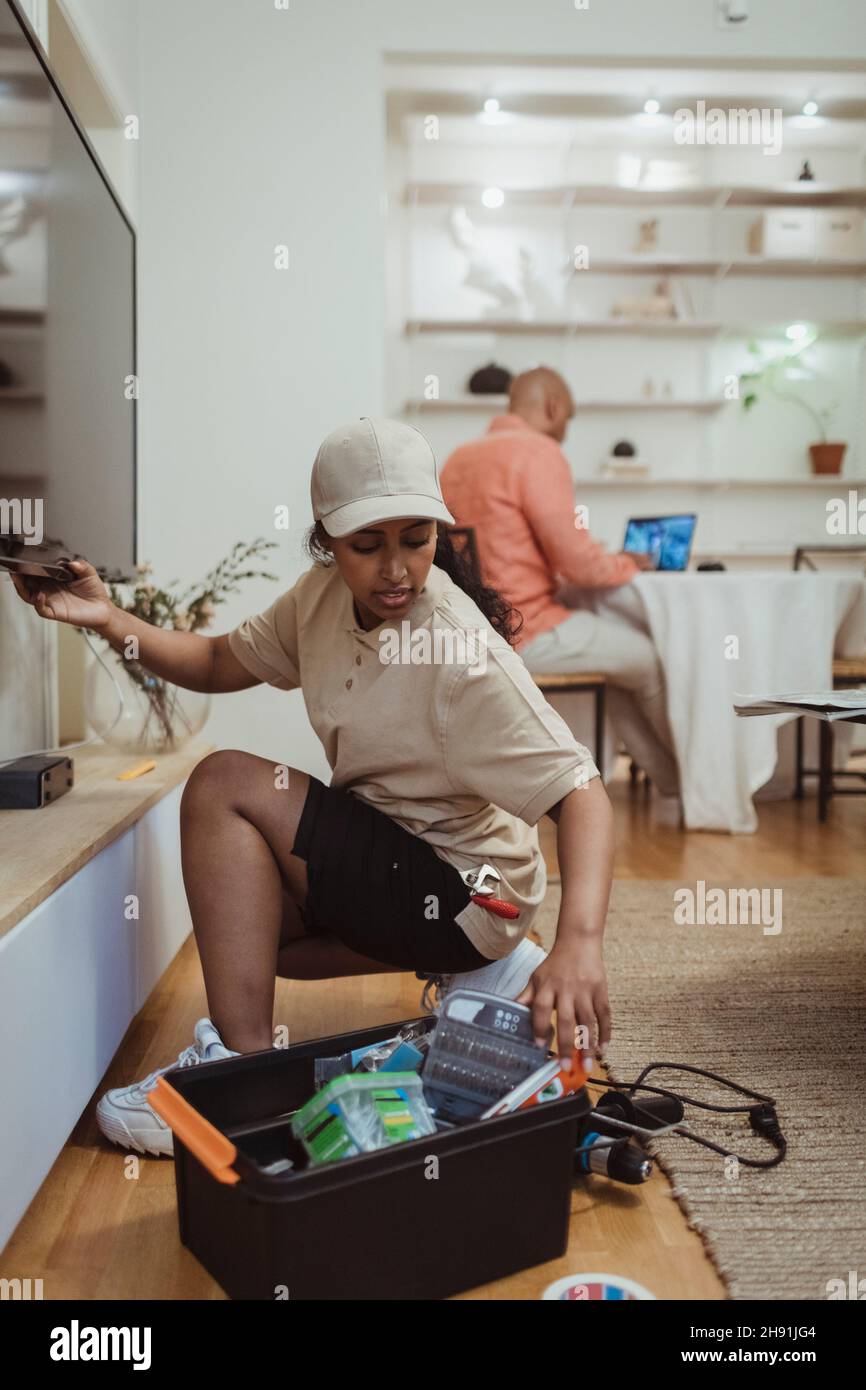 Femme ingénieur de maintenance qui installe le téléviseur dans le salon Banque D'Images