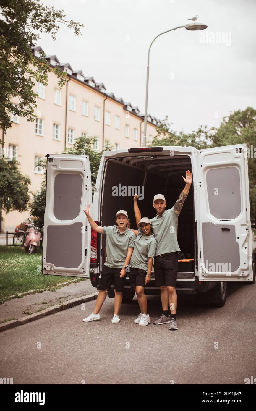 Joyeux collègues de sexe féminin et masculin avec les mains soulevées contre la camionnette de livraison Banque D'Images