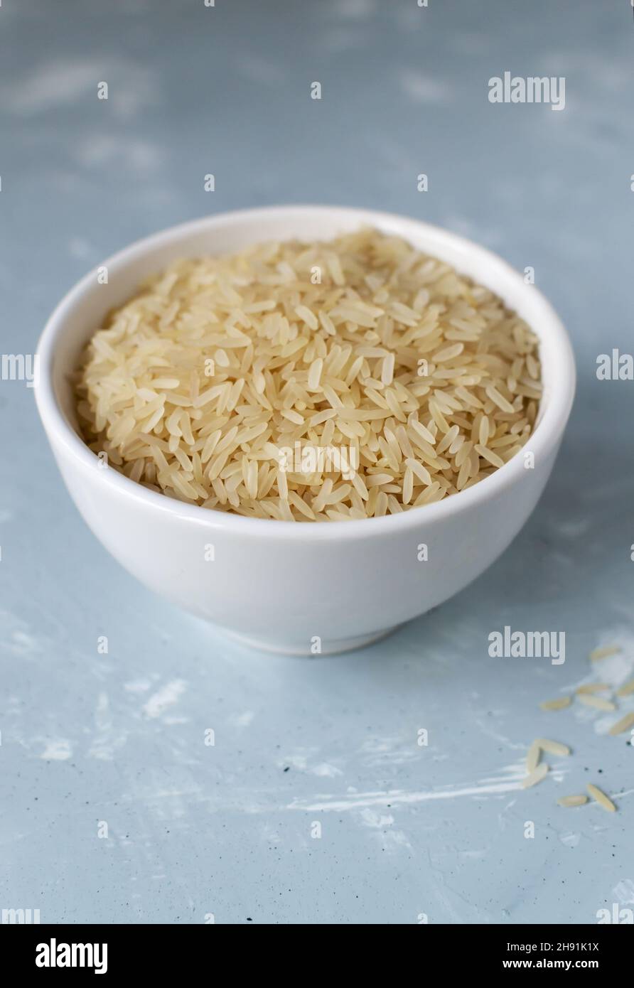 Séchez le riz dans un bol blanc sur fond gris.Concept de saine alimentation.Orientation verticale.Les plats de riz sont cuits dans tous les pays du monde.Pop Banque D'Images