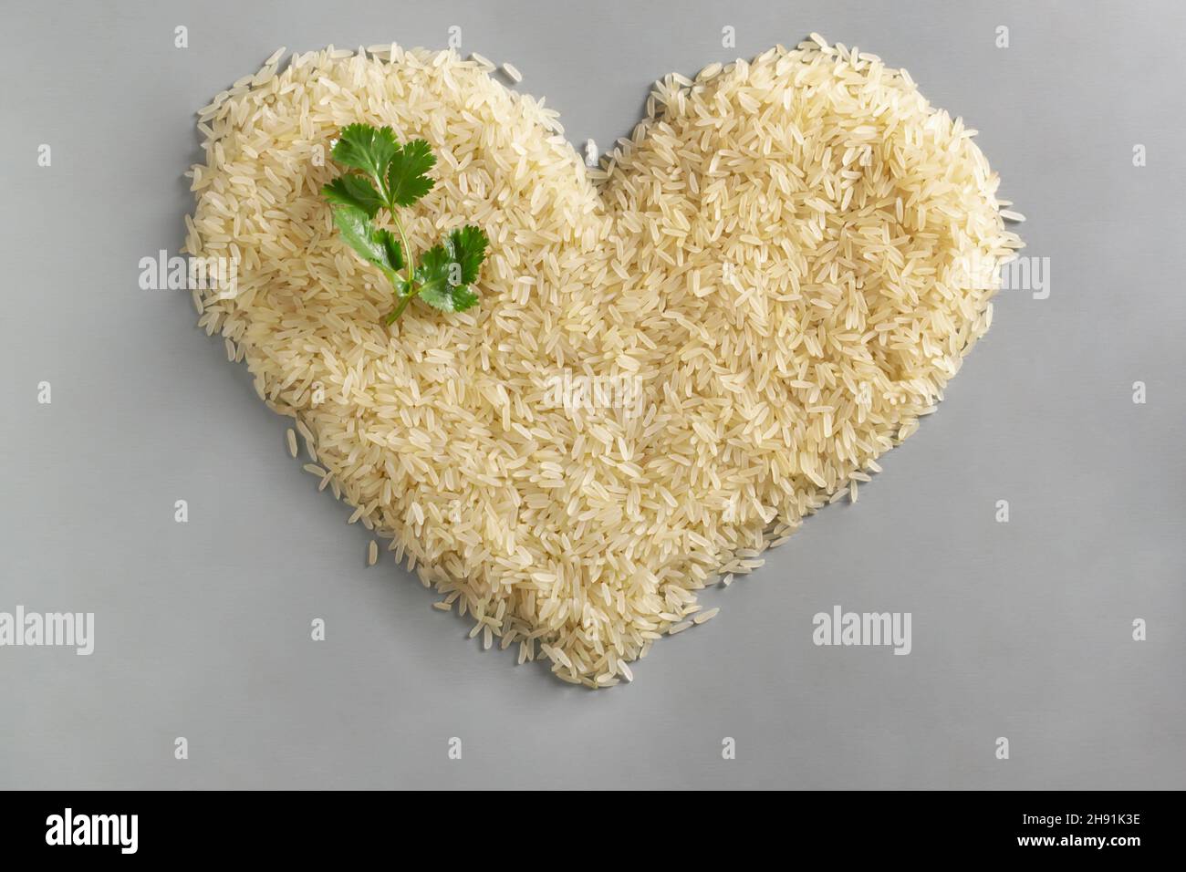 Le riz blanc à grain long est disposé en forme de coeur avec une branche verte de coriandre.Concept d'alimentation saine.Les plats de riz sont cuits dans tous les pays Banque D'Images