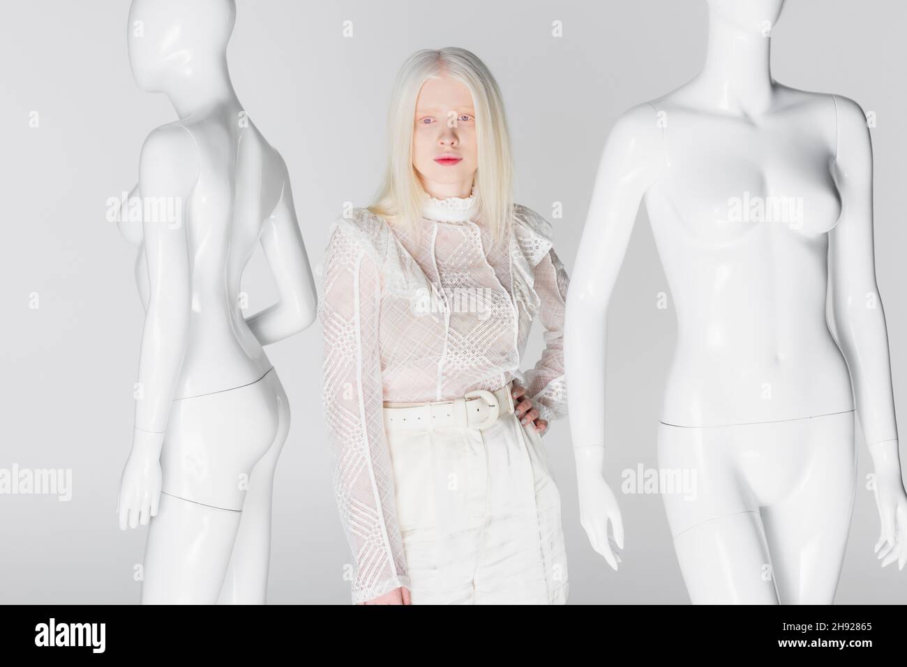 Femme blonde et albinos avec main sur la hanche près des mannequins isolés sur blanc Banque D'Images