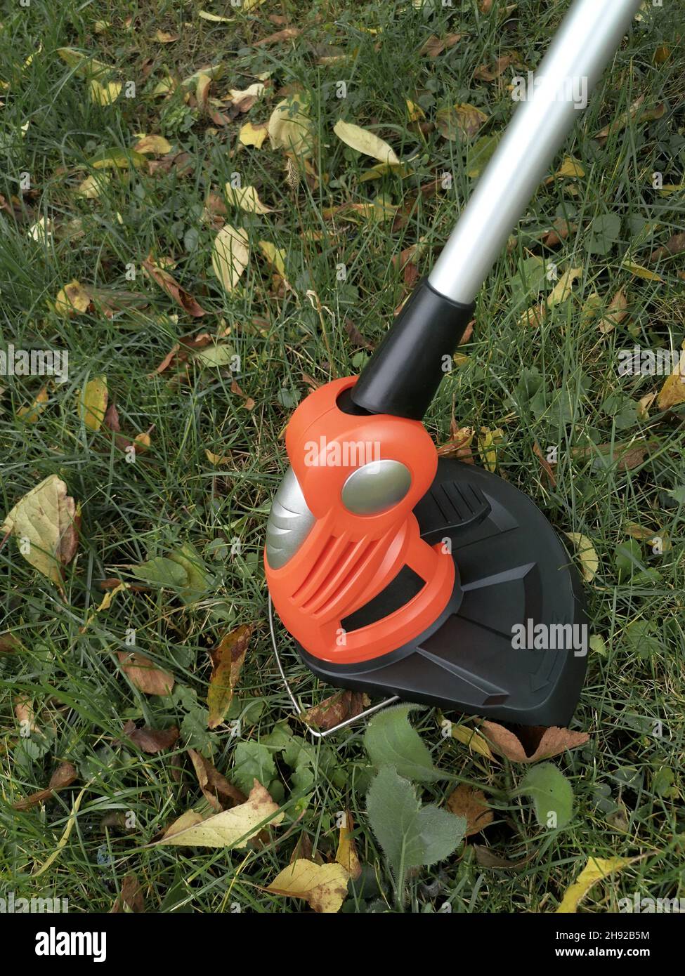Appareils électroménagers : tondeuse-tondeuse pour couper des pelouses sur des batteries rechargeables.Présenté sur un fond d'herbe et de feuilles, vue avant, Banque D'Images