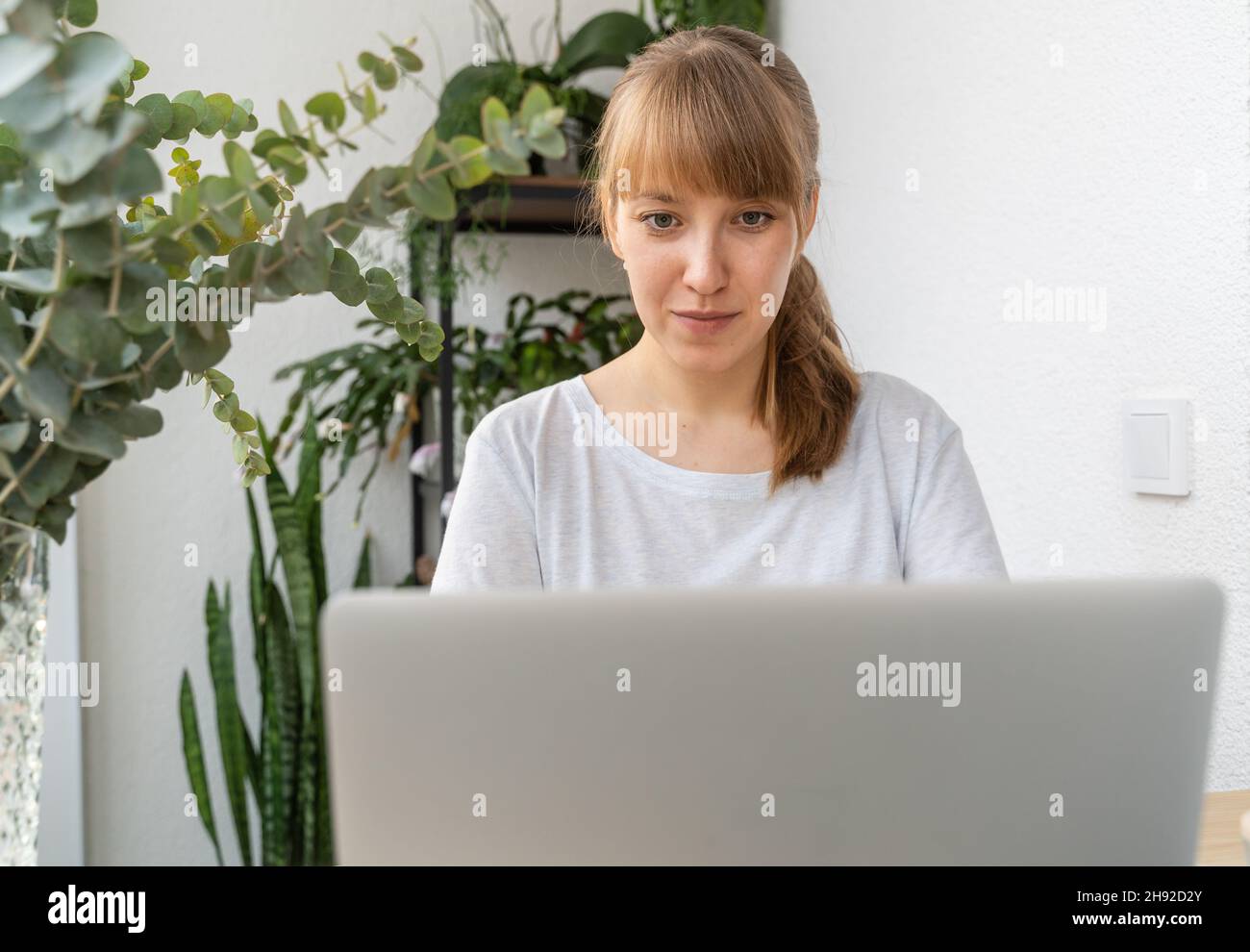 Femme travaillant sur un ordinateur portable entouré de plantes et de fleurs sur le balcon pendant la journée Banque D'Images