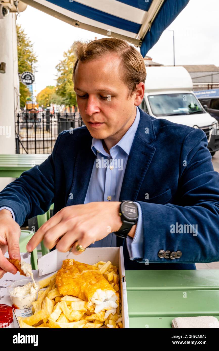 Un jeune homme bien habillé mangeant Un repas de poisson et de puce, Londres, Royaume-Uni. Banque D'Images