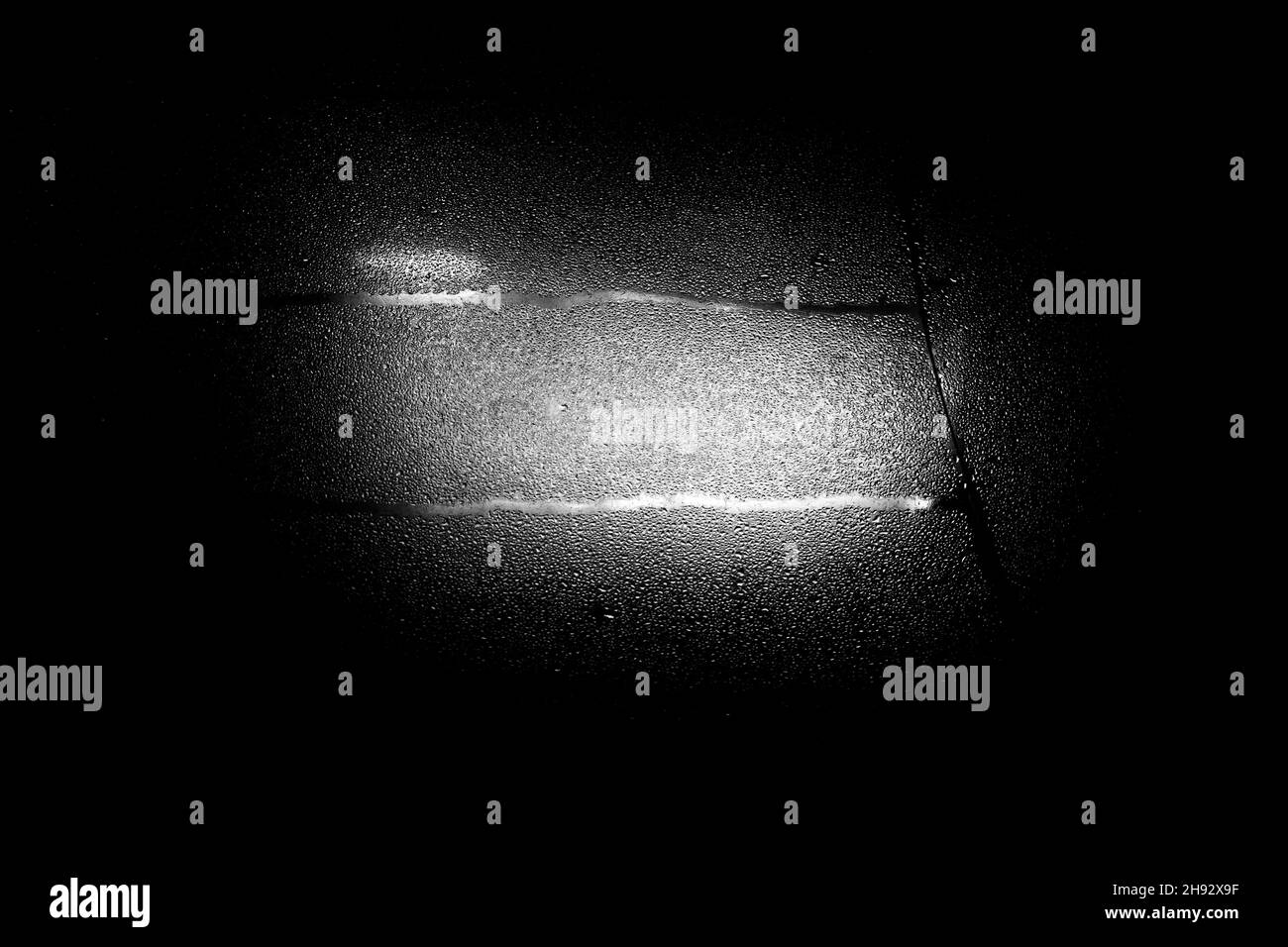 Un spot blanc de lumière à travers le vieux verre dans l'obscurité sur un fond noir. Banque D'Images