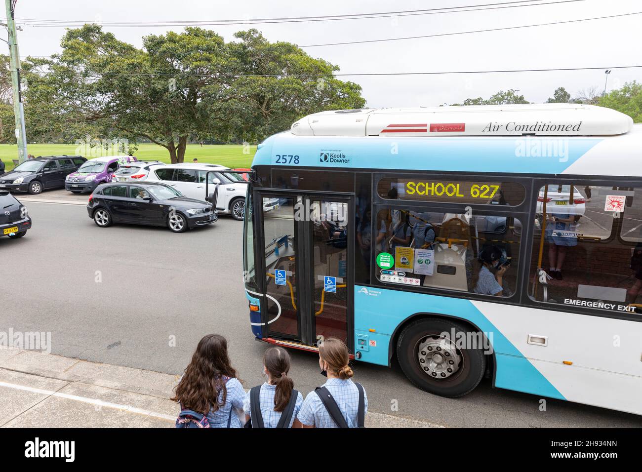 Année australienne 12 jeunes filles à l'arrêt d'autobus scolaire comme autobus scolaire arrive,Sydney,NSW,Australie Banque D'Images