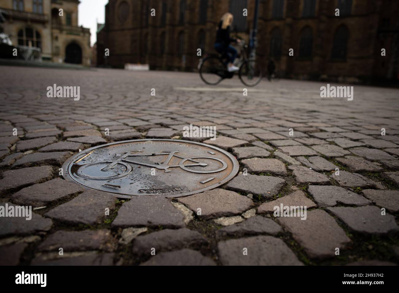 Gros plan d'une plaque métallique avec un symbole de vélo sur la chaussée de Brême, Allemagne avec des cyclistes en arrière-plan démontrant la mobilité active Banque D'Images