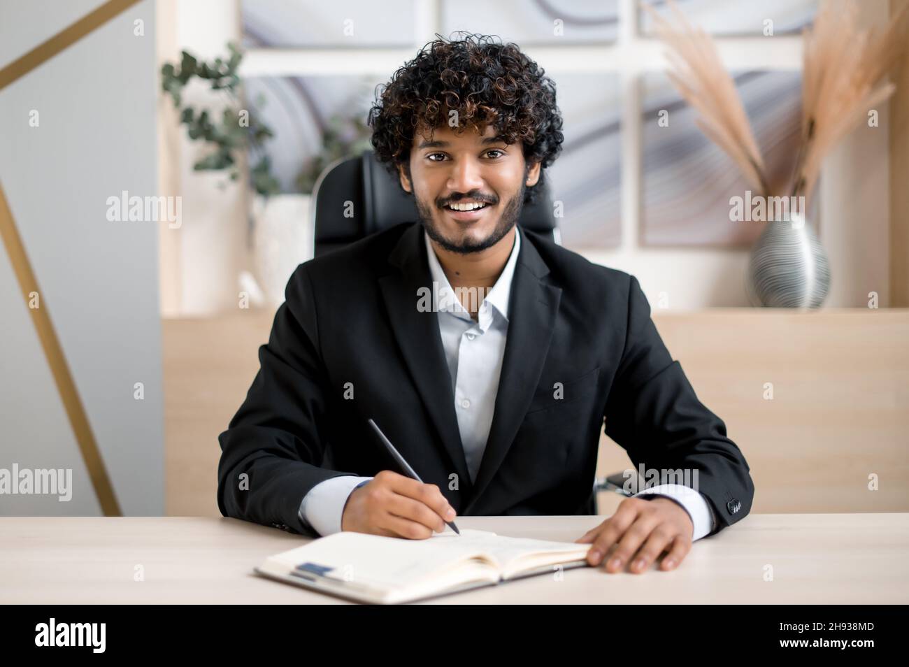 Amical positif personne d'affaires, mentor ou étudiant indien réussi, en parlant avec un collègue ou un client lors d'une conférence téléphonique, en entrevue en ligne, regarde la caméra, prend des notes, sourit.E-learning Banque D'Images