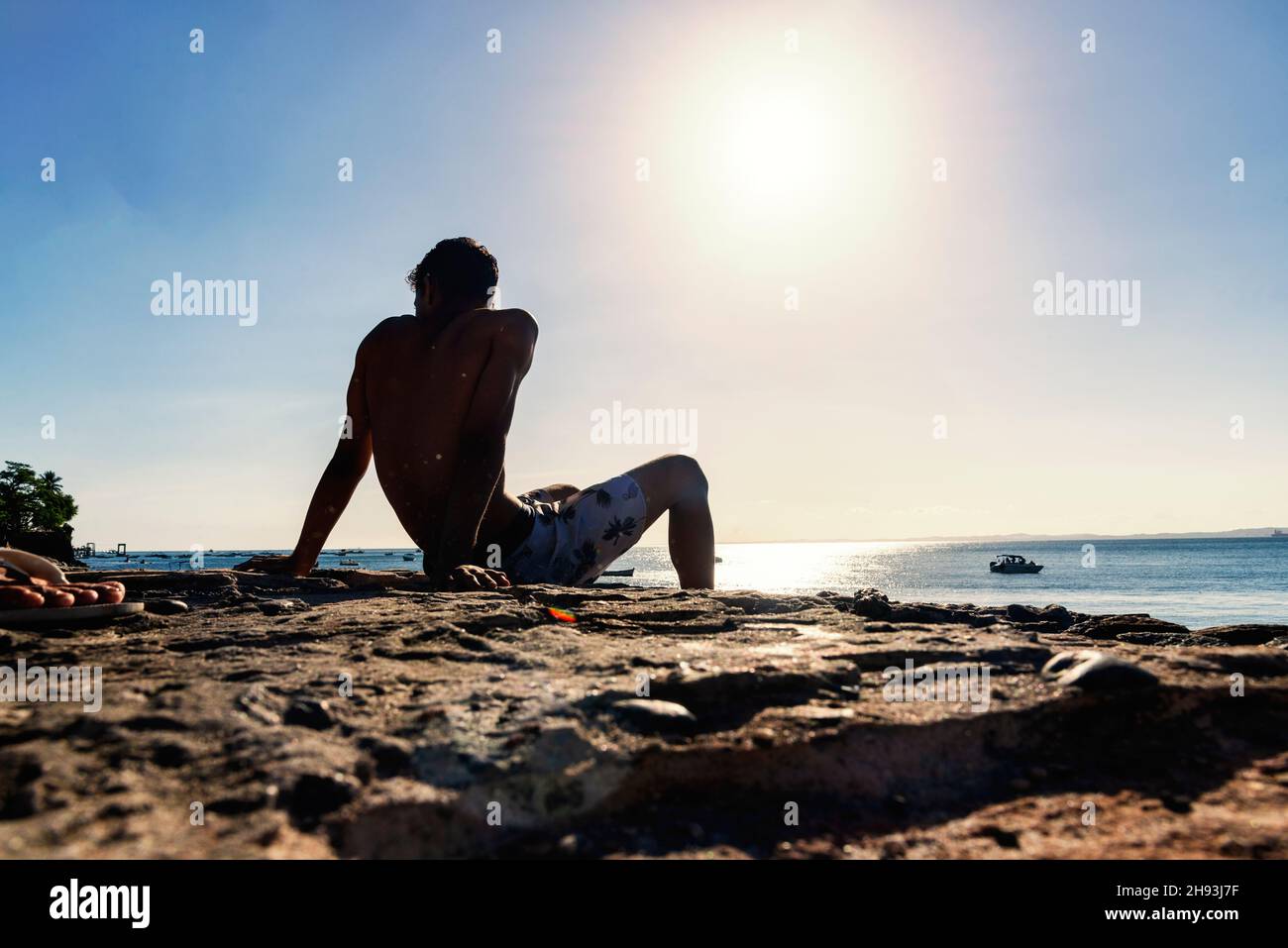 Une personne assise près de la mer contre la lumière du soleil.Salvador, Bahia, Brésil. Banque D'Images