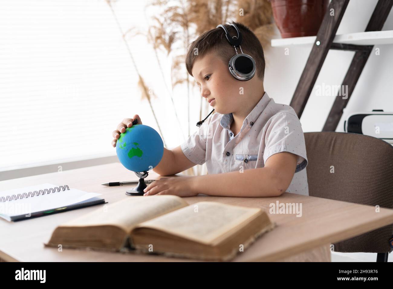 Un garçon d'école triste assis dans un casque à un bureau écoute une leçon de géographie et regarde le monde, étudiant la countrie et l'océan.Sans fil Banque D'Images