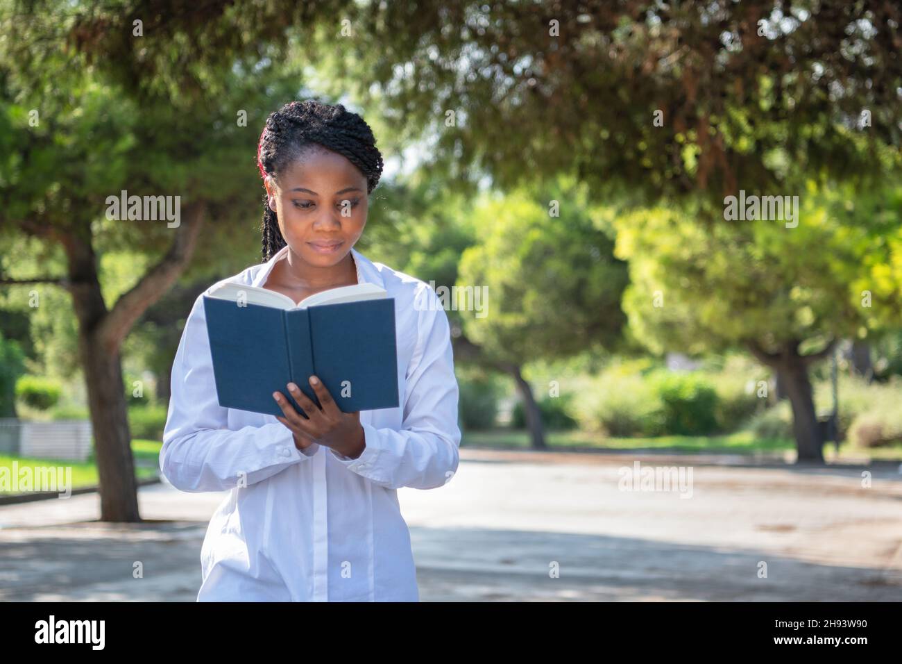 Jeune femme debout dans un parc tout en lisant un livre Banque D'Images
