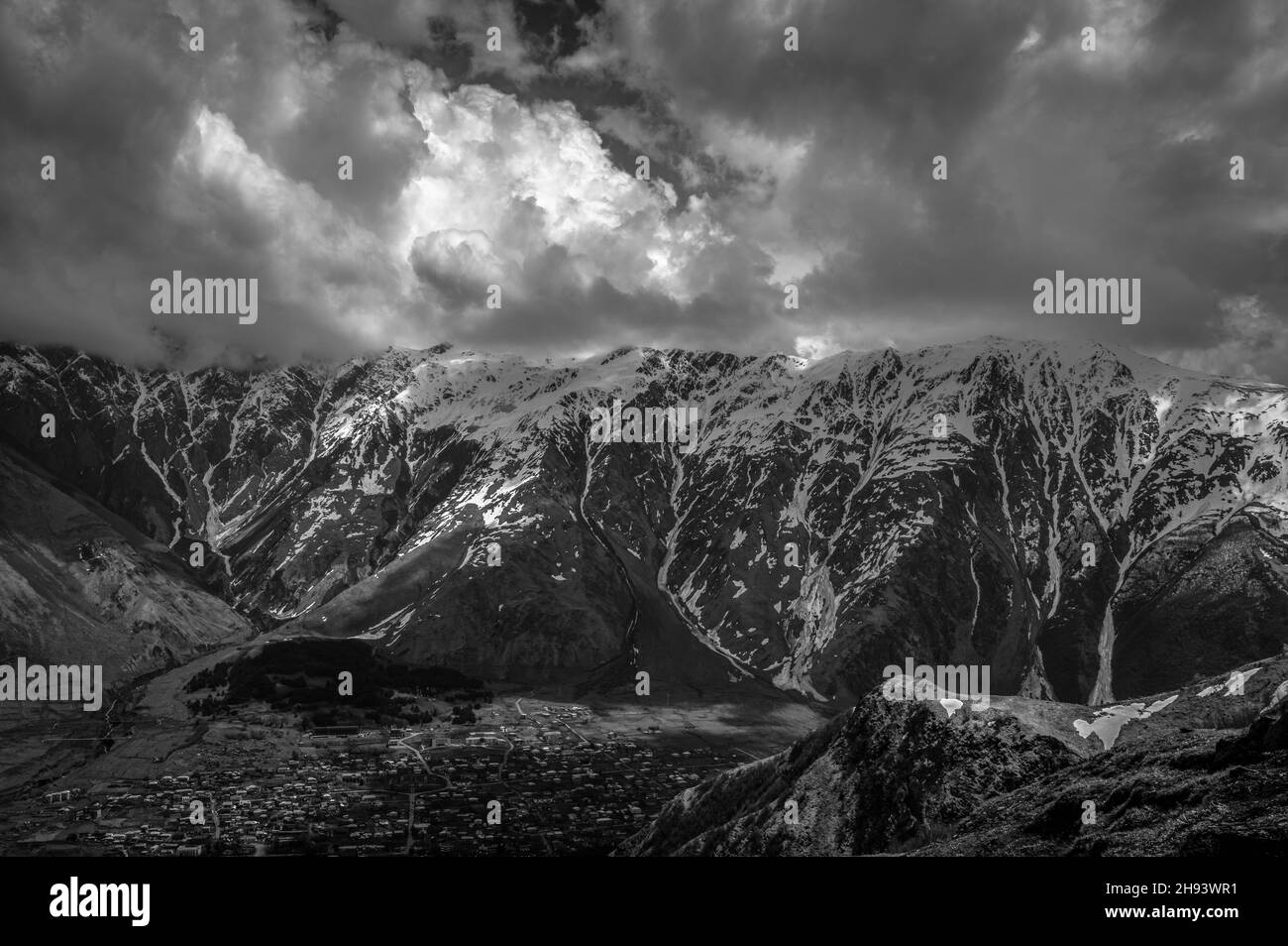 Vue panoramique des montagnes du Grand Caucase et de la ville de Stepantsminda (Kazbegi) contre ciel nuageux, Géorgie.Noir et blanc. Banque D'Images