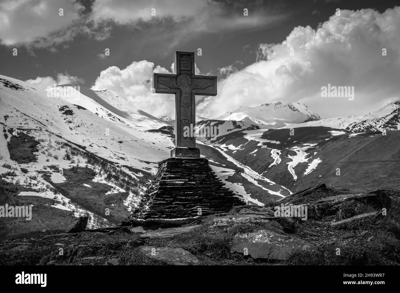 Vue panoramique d'une croix géorgienne sur le sommet de la montagne contre les glaciers et ciel bleu nuageux.Stepantsminda (Kazbegi), Géorgie.Noir et blanc. Banque D'Images