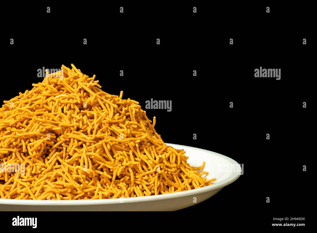 Tas de Spicy Sev Namkeen Food dans un plat blanc sur le côté droit, farine de pois chiches et épices, isolé dans un fond noir Banque D'Images