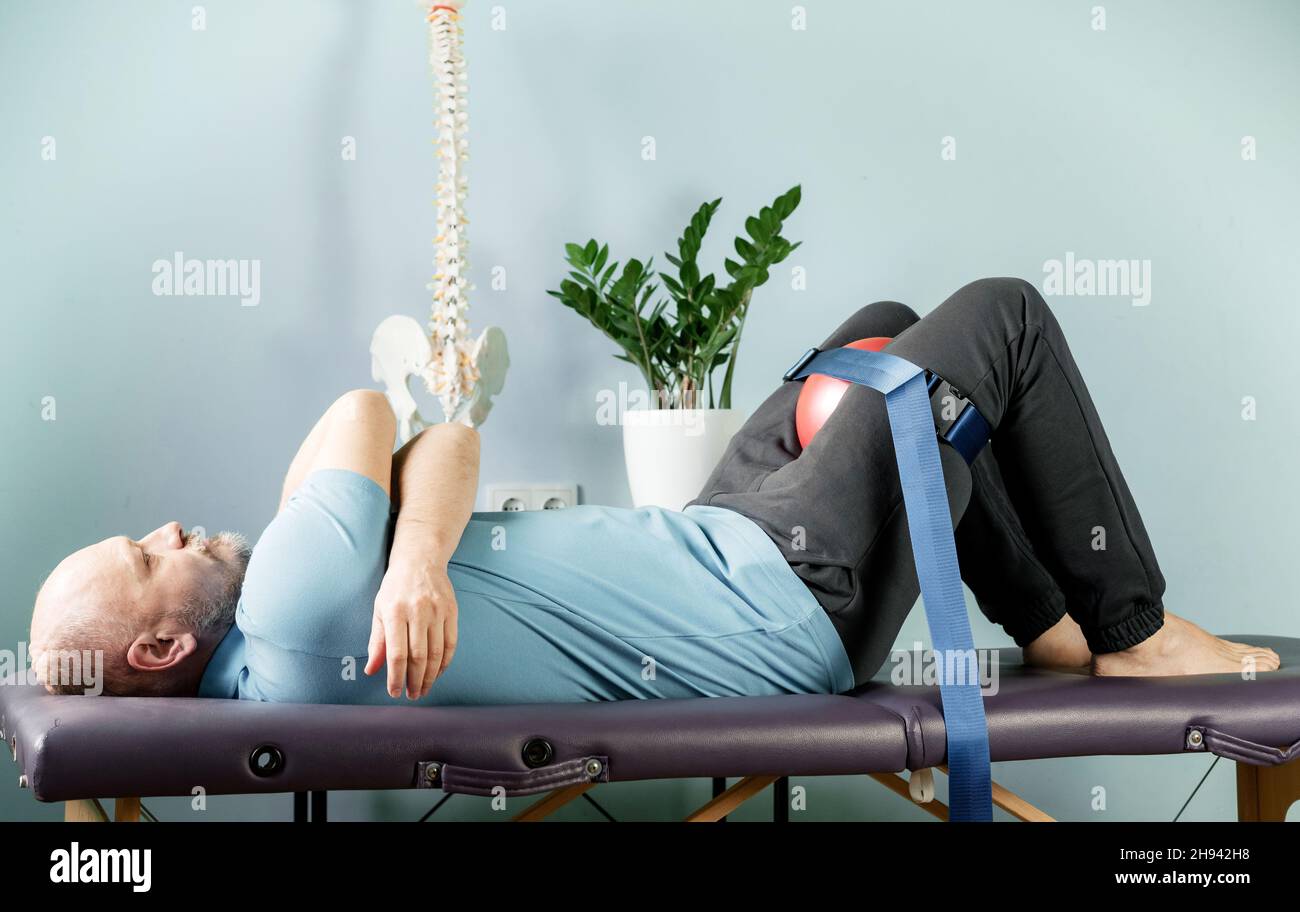 Un homme allongé sur la table de massage en position de repos constructive avec un rouleau en mousse et une ceinture de maligan Banque D'Images