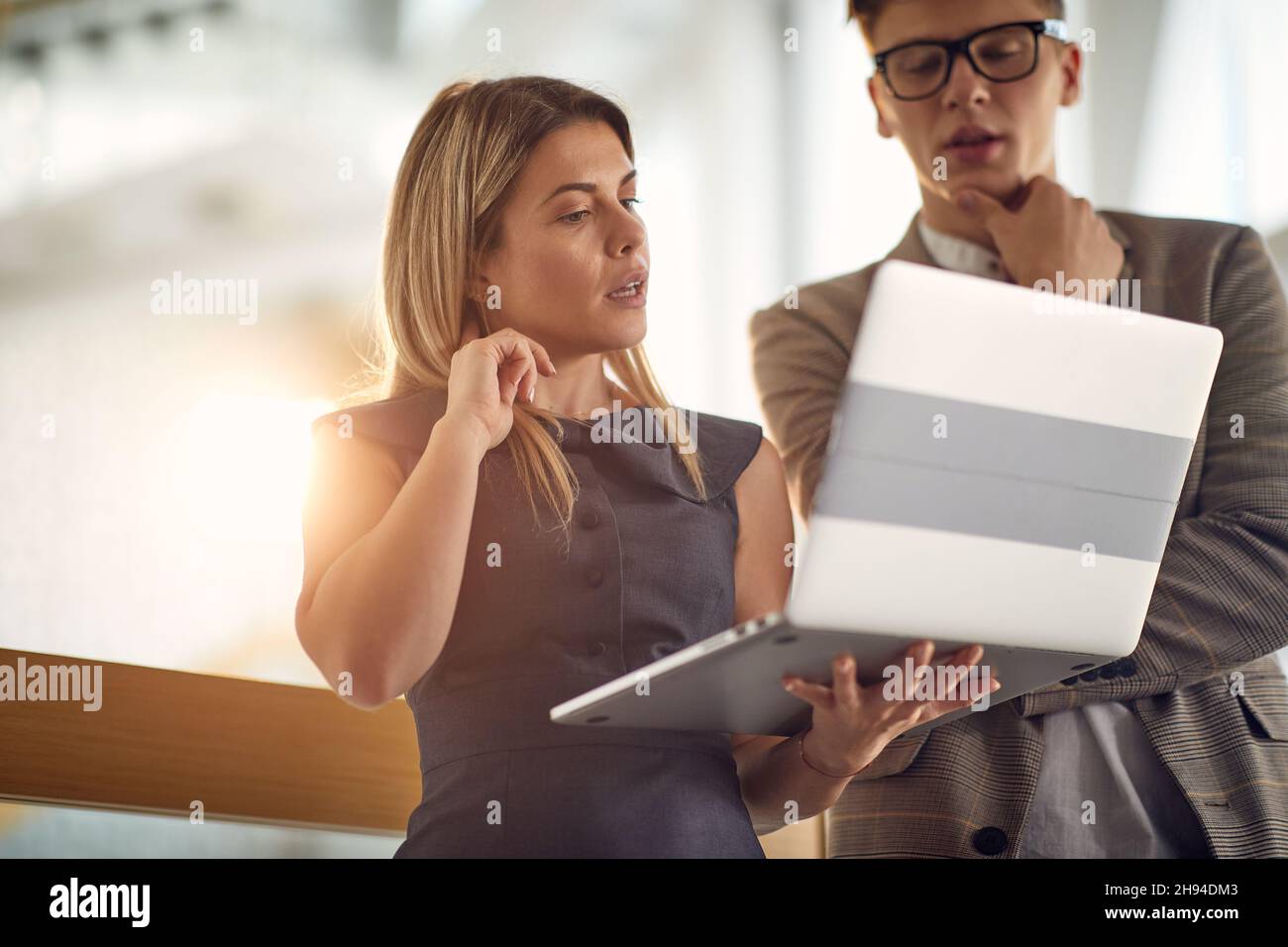 Une jeune femme d'affaires et son jeune collègue sont debout dans le couloir et se concentrent sur un contenu d'ordinateur portable qu'ils regardent ensemble Banque D'Images