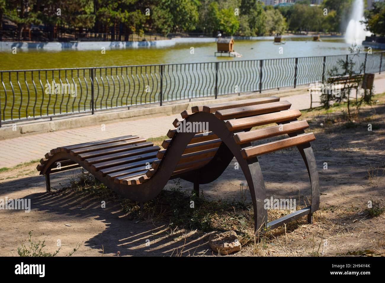 Un banc décoratif incurvé en bois fait de planches se tient dans un parc d'été vide Banque D'Images