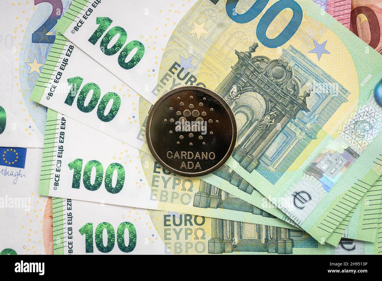 Cardano Ada pièce de monnaie physique qui s'élève au-dessus des factures de 100 euros. Banque D'Images