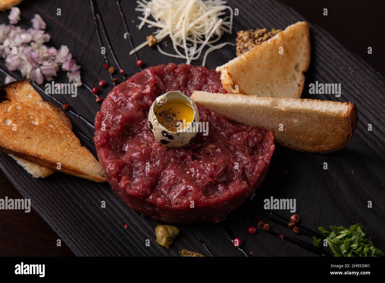 Tartare de bœuf avec œuf de caille et pain blanc grillé sur une assiette élégante noire Banque D'Images